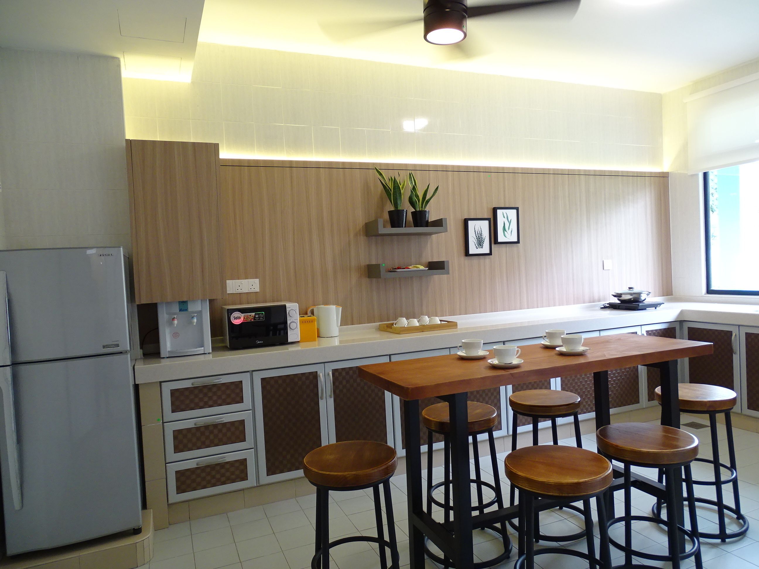 Una cocina moderna con una isla central, taburetes de bar, un refrigerador y una ventana con luz natural.