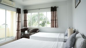 Habitació d'hotel amb dos llits, una finestra amb cortines, una cadira, una taula i un aparell d'aire condicionat.
