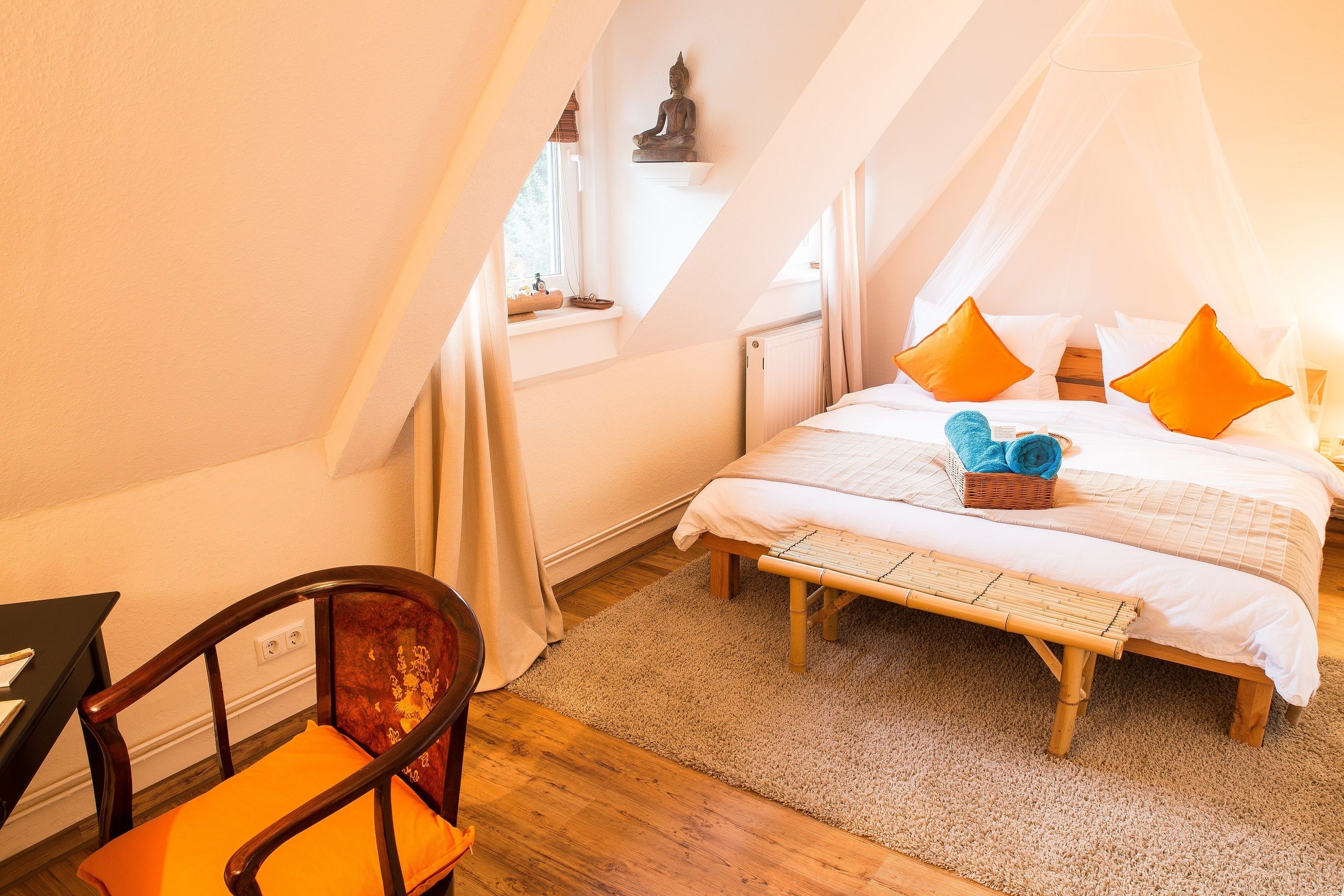 A bedroom with a bed, a chair, a window, and a statue.