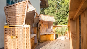 Een houten terras met rieten meubilair en gestreepte zonneschermen.