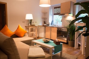 Un espacio habitable compacto con sofá, una mesita, una cocina con estufa y una planta en maceta.