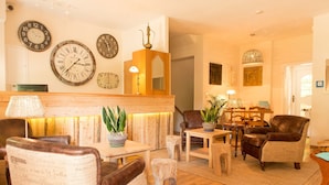 Een gezellige lobby met leren fauteuils, een houten receptiebalie en diverse klokken aan de muur.