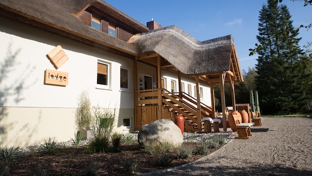 Een lodge met rieten dak, houten veranda en een zitgedeelte buiten.