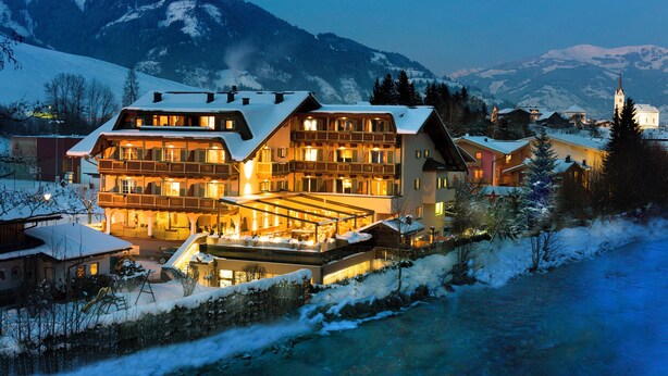 A multi-story hotel with balconies, a covered outdoor area, and a view of snow-covered mountains. - Hotel Kaprunerhof (Kaprun)