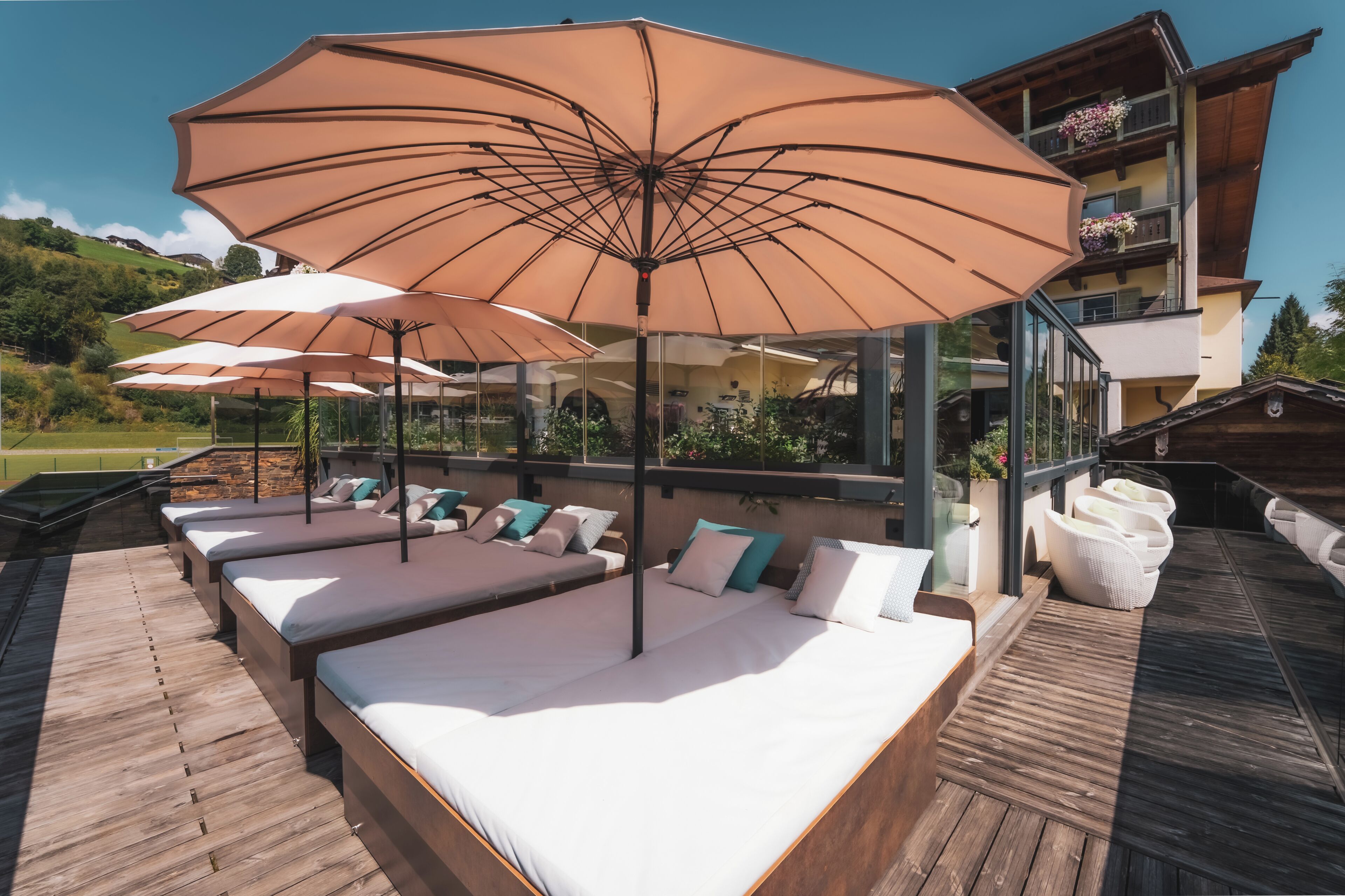 A rooftop lounge with multiple sunbeds and large umbrellas, overlooking a scenic landscape.