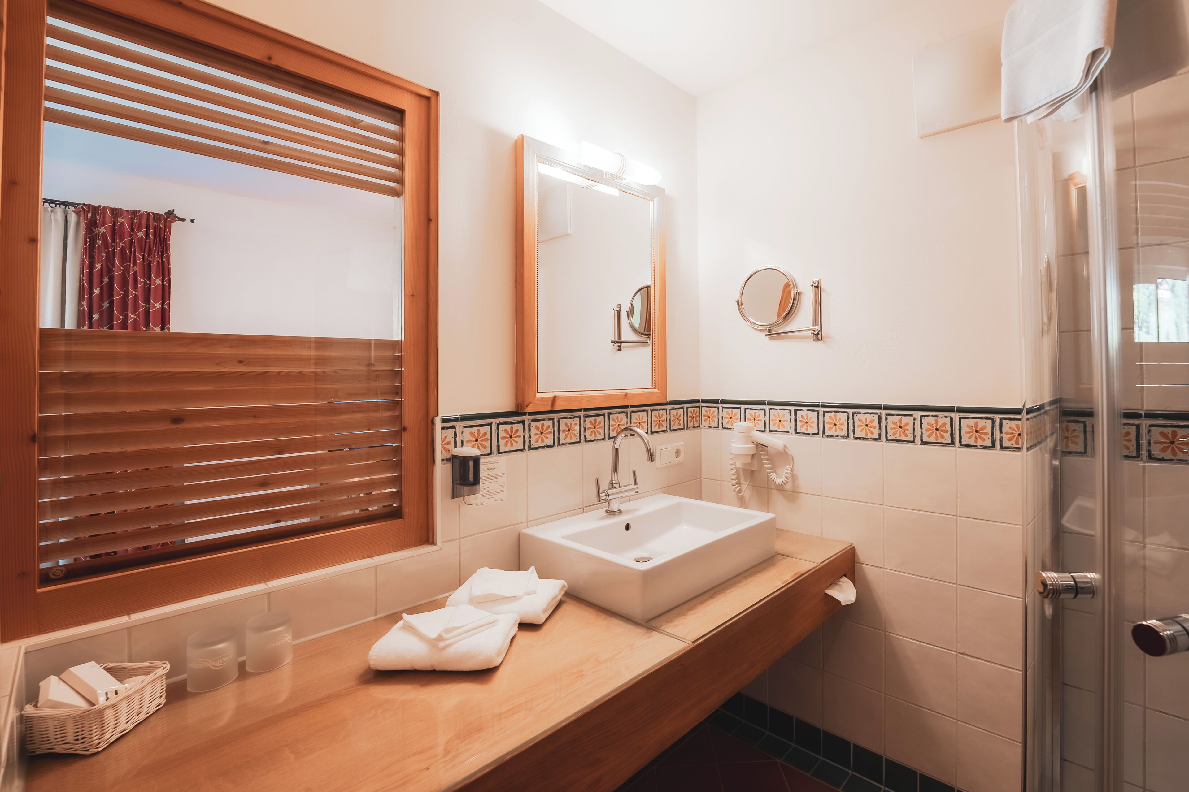Un baño con tocador de madera, un espejo grande, un lavamanos y una zona de ducha.
