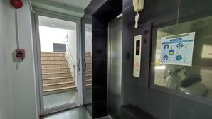 A hotel lobby with a fire alarm, a welcome mat, a digital elevator control panel, and a COVID-19 informational poster.