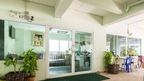 A room with a sliding glass door leading to a kitchen area, a green mat at the entrance, and several potted plants.