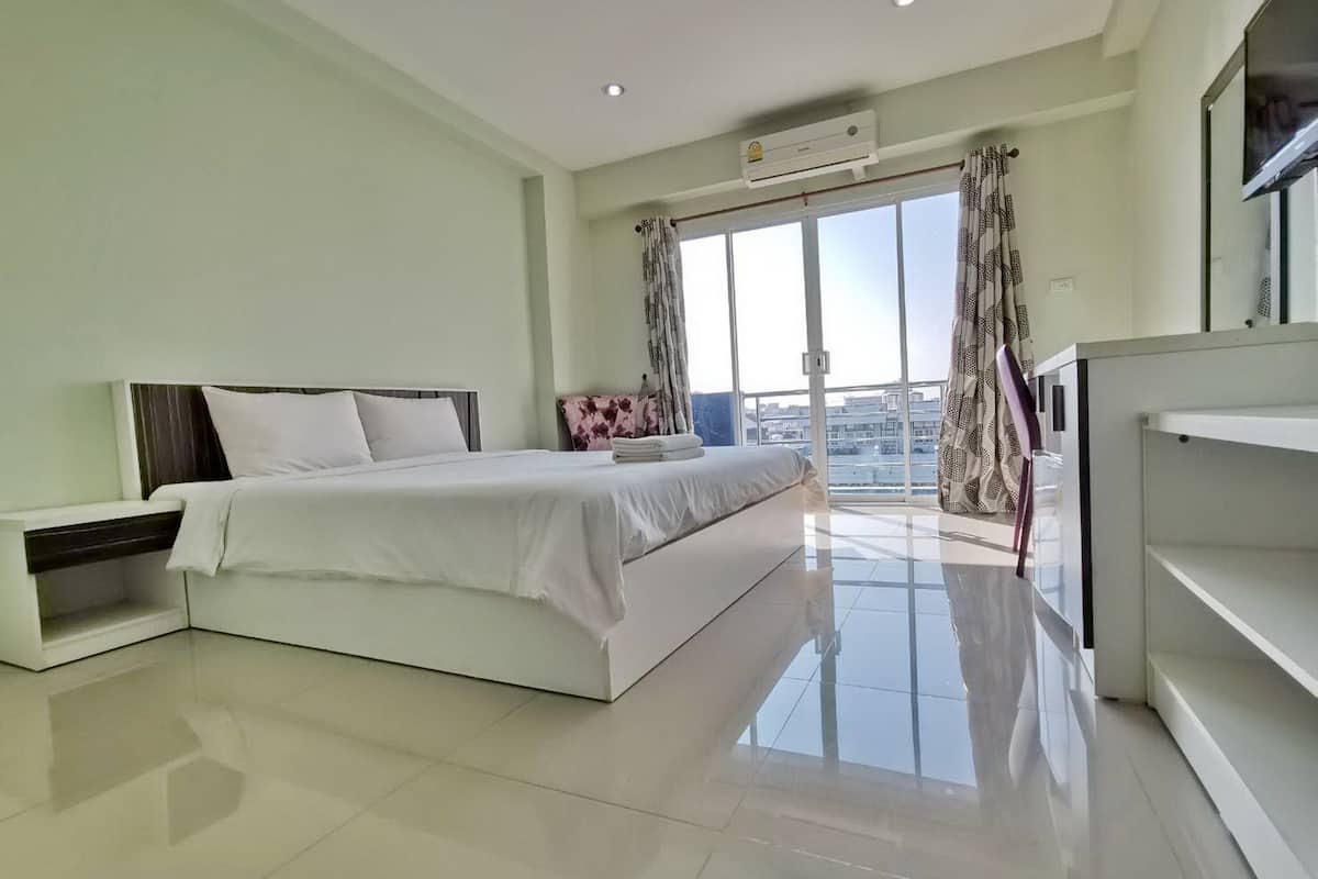A modern bedroom with a large bed, a TV, and a balcony with curtains.