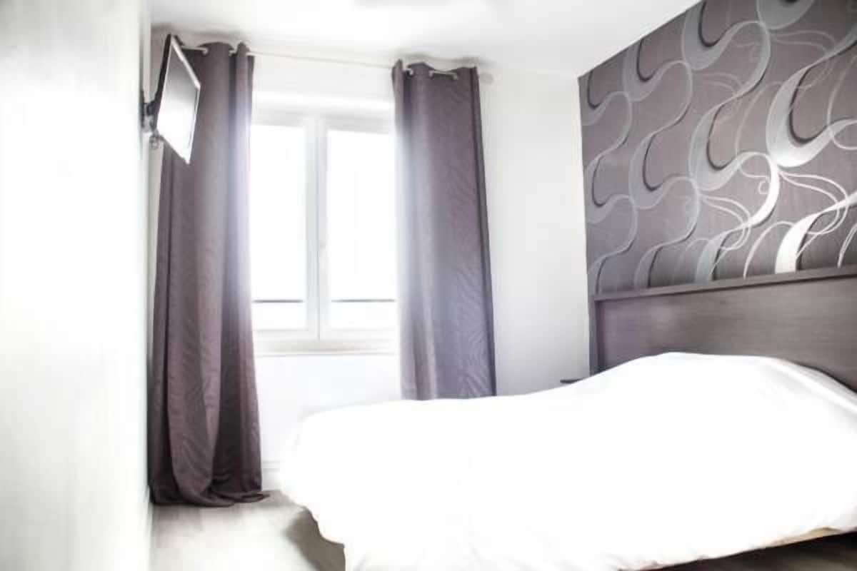 A bedroom with a bed, curtains, a window, and a wall with a wavy pattern.