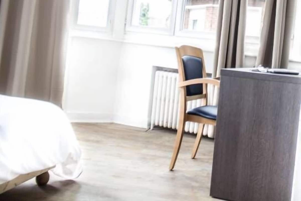 A hotel room with a bed, a chair, a desk, and a window with curtains.