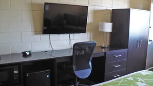 A hotel room with a bed, a desk with a chair, a TV mounted on the wall, a cabinet, and a lamp. - Westgate Inn (Portage La Prairie)