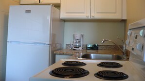 A kitchen with white cabinets, a refrigerator, a coffee maker, a stove, and a sink. - Westgate Inn (Portage La Prairie)