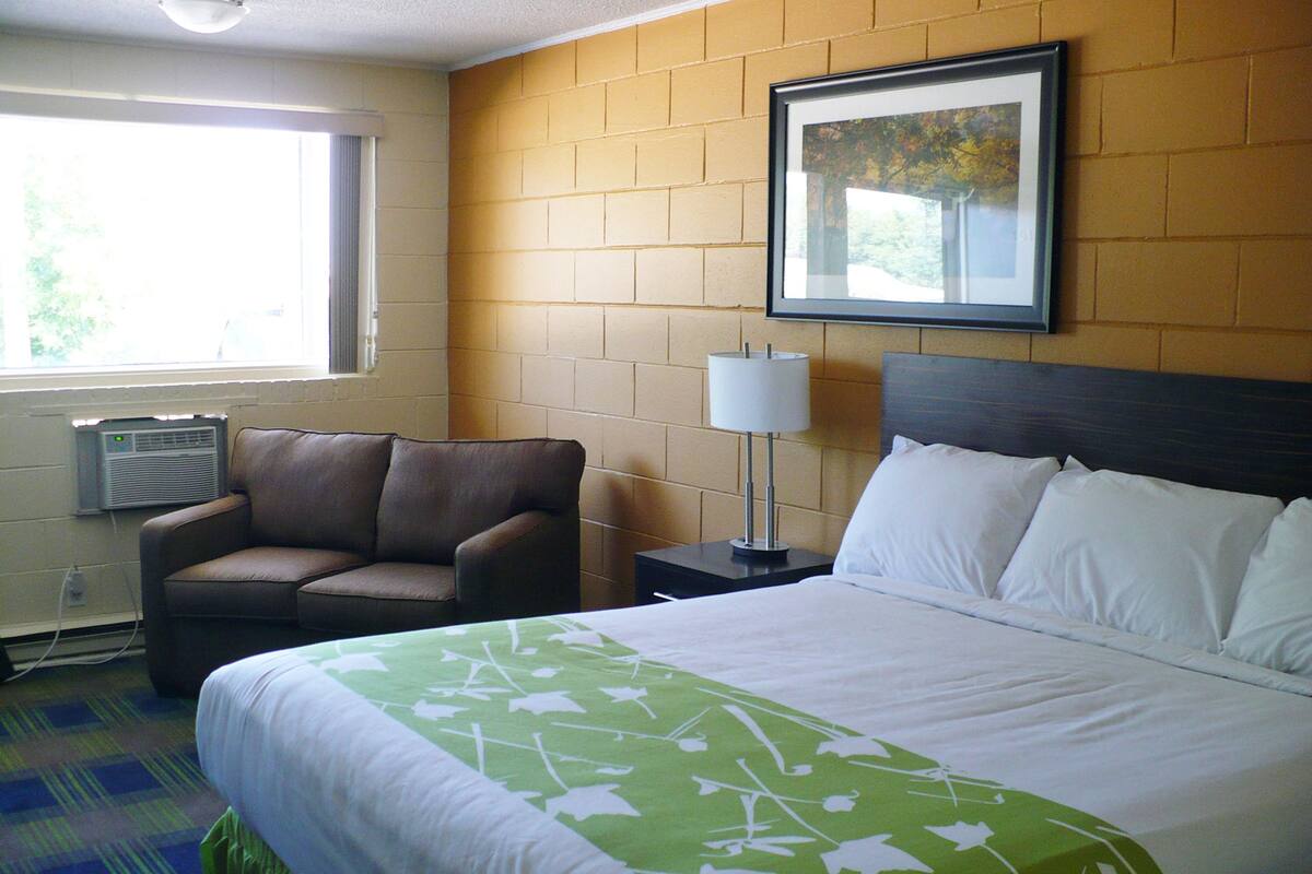 Une chambre d’hôtel avec un lit, une chaise, une table de chevet, une lampe et un tableau au mur.