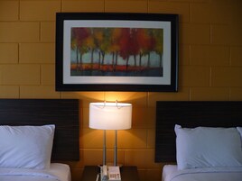 Una habitación de hotel con dos camas, un cuadro enmarcado sobre ellas y una lámpara de noche.