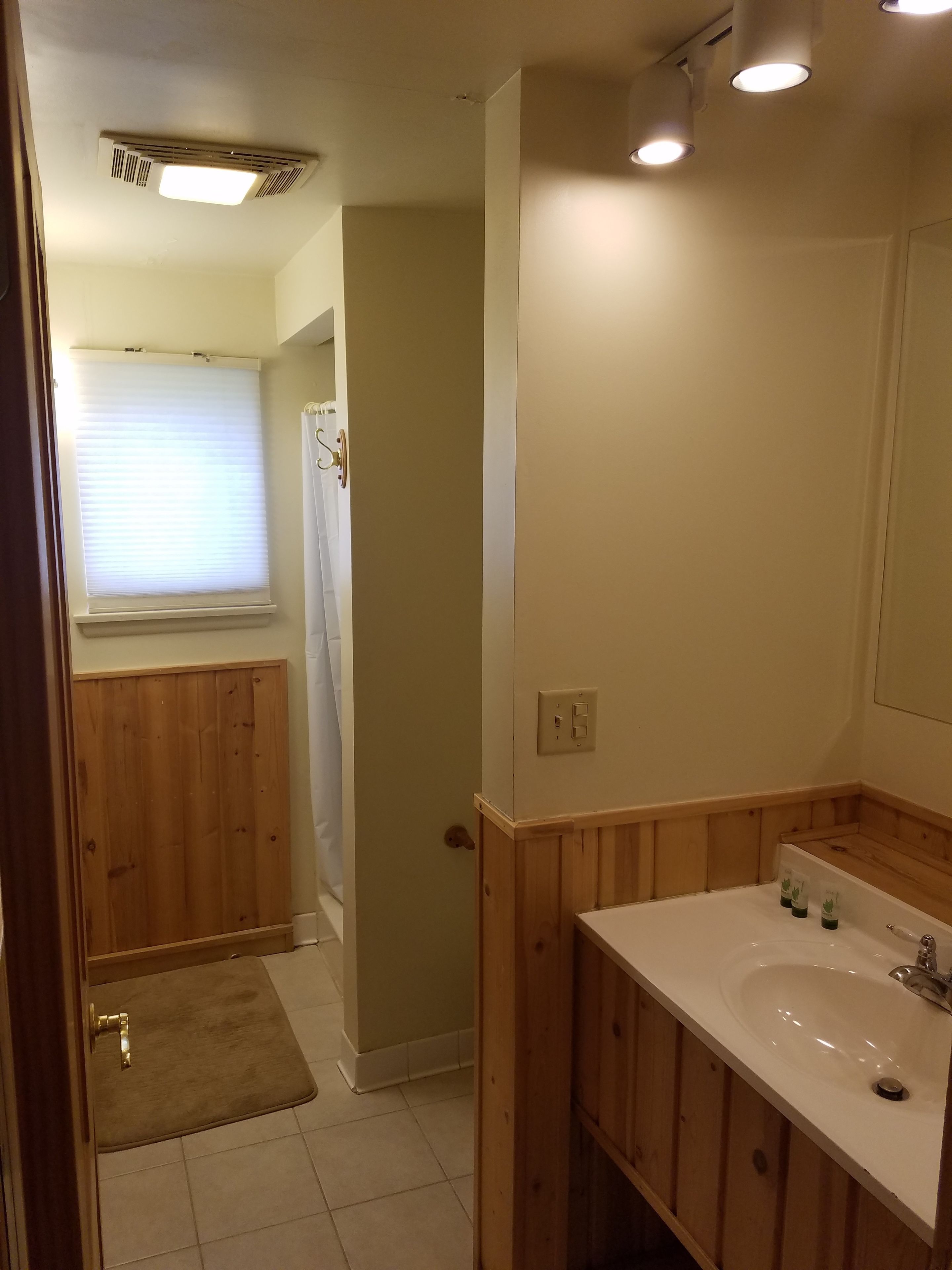 A bathroom with wooden paneling, a white sink, and a window with blinds.