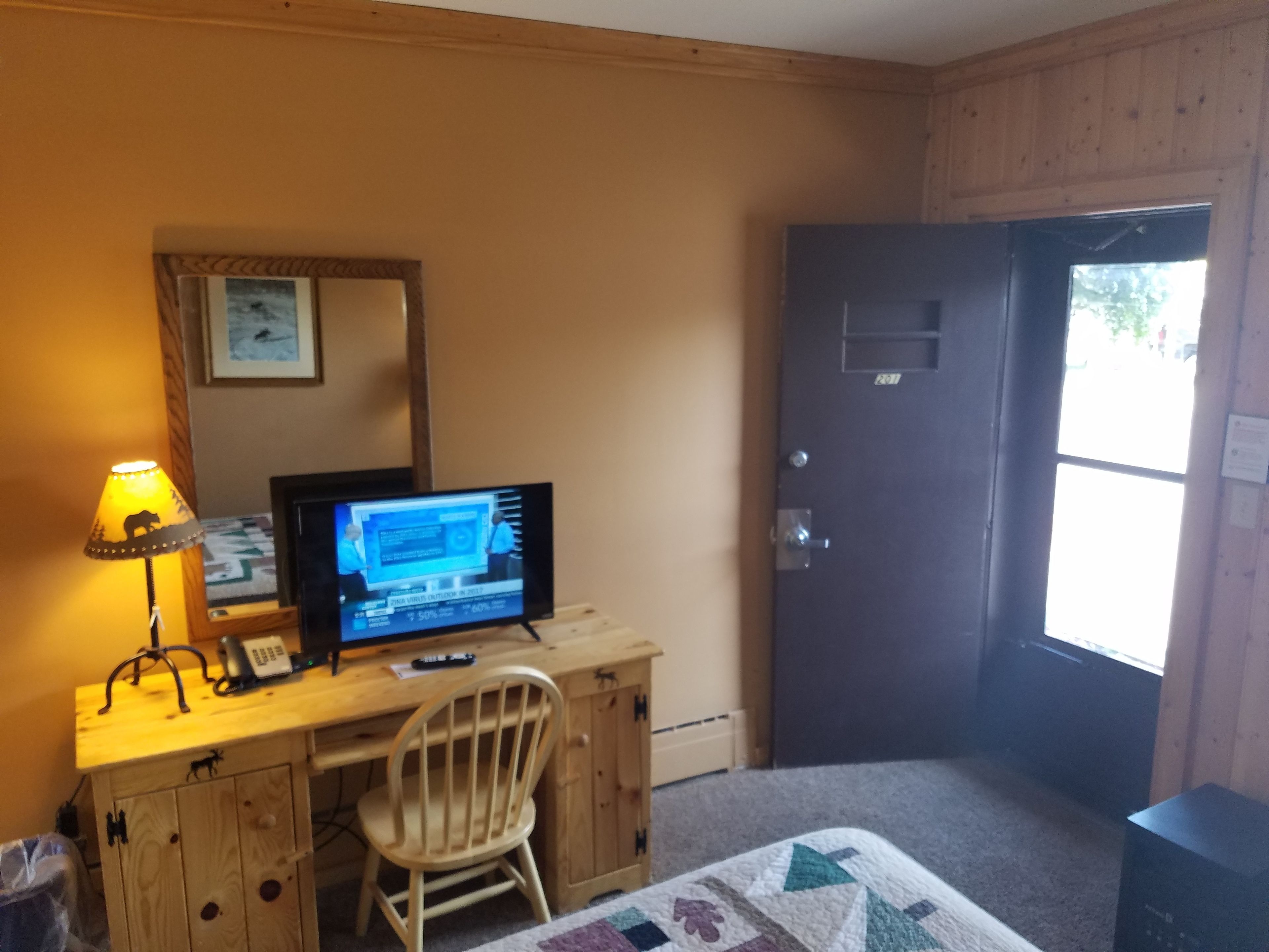 A wooden desk with a computer, a lamp, and a chair in a room with a door and a window.