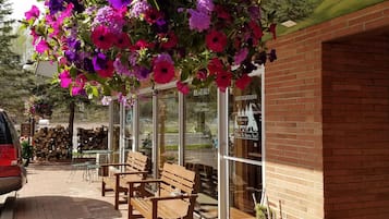 A brick building with a hanging flower display, wooden benches, and a car parked outside.