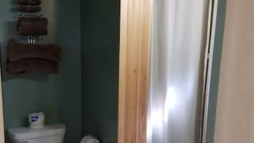 A bathroom with a toilet, a wooden panel, a shower curtain, and a towel rack with towels.