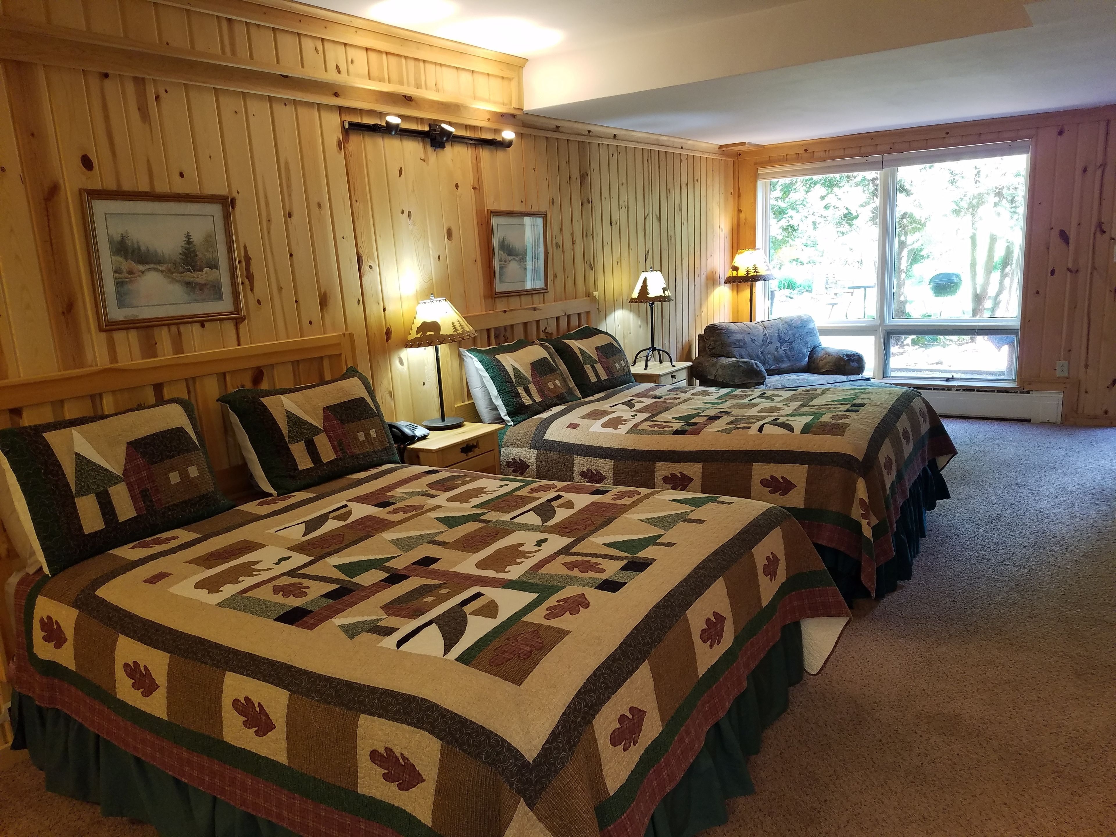 Una habitación con dos camas, paredes de madera y ventanas amplias.