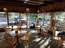 Un restaurante con interior de madera, ventanas grandes y mesas al aire libre.