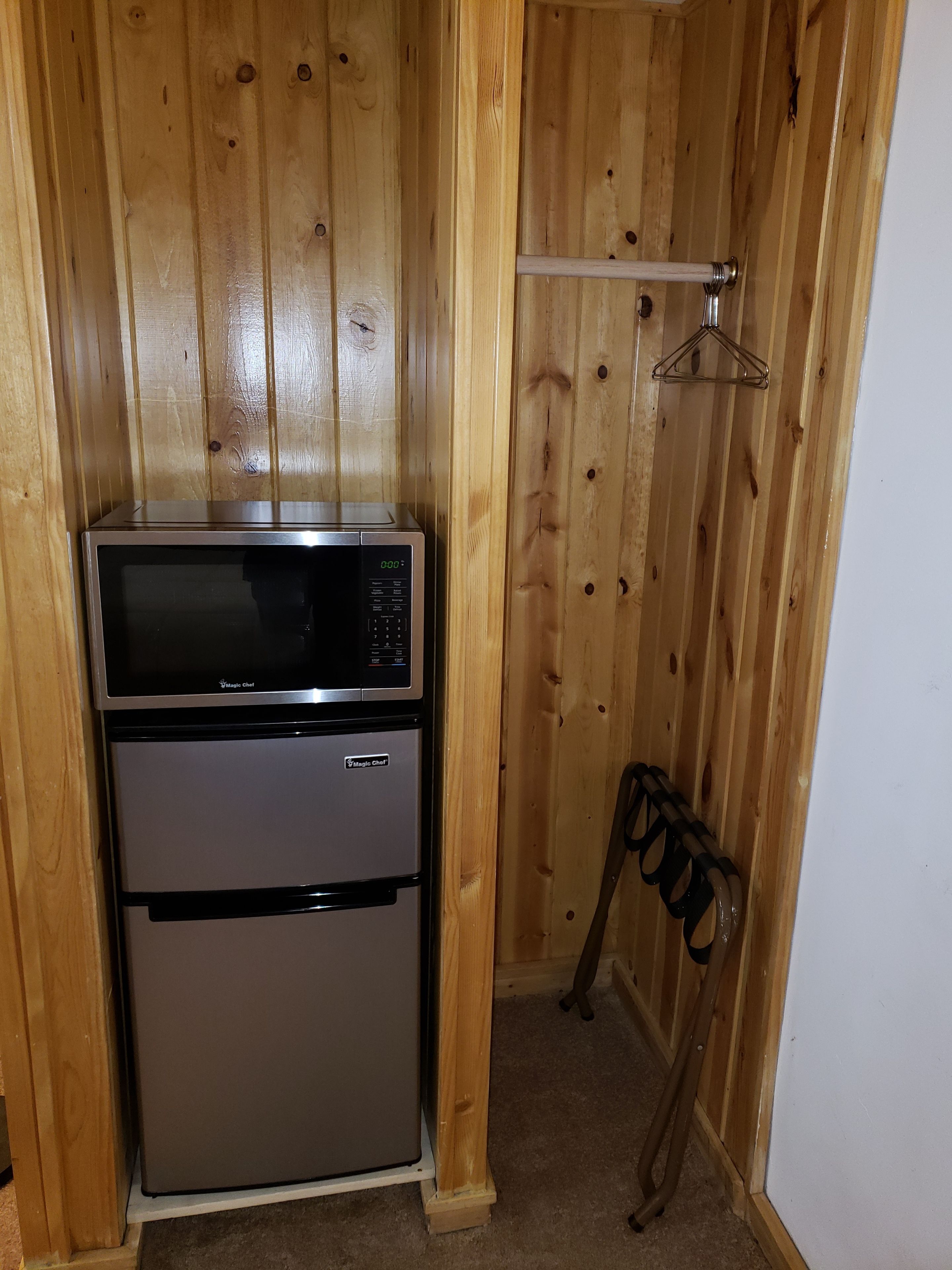 Uma cozinha compacta equipada com micro-ondas e frigorífico, paredes em painel de madeira e um porta-casacos.