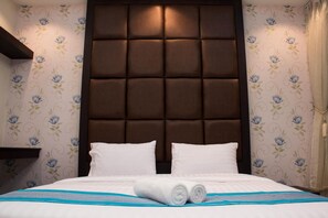 A neatly made bed with white linens and two pillows, a brown padded headboard, and floral wallpaper. - Roses Hua Hin Hotel (Hua Hin)