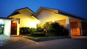 A modern building with a well-lit entrance, a covered porch, and a gated driveway. - Roses Hua Hin Hotel (Hua Hin)