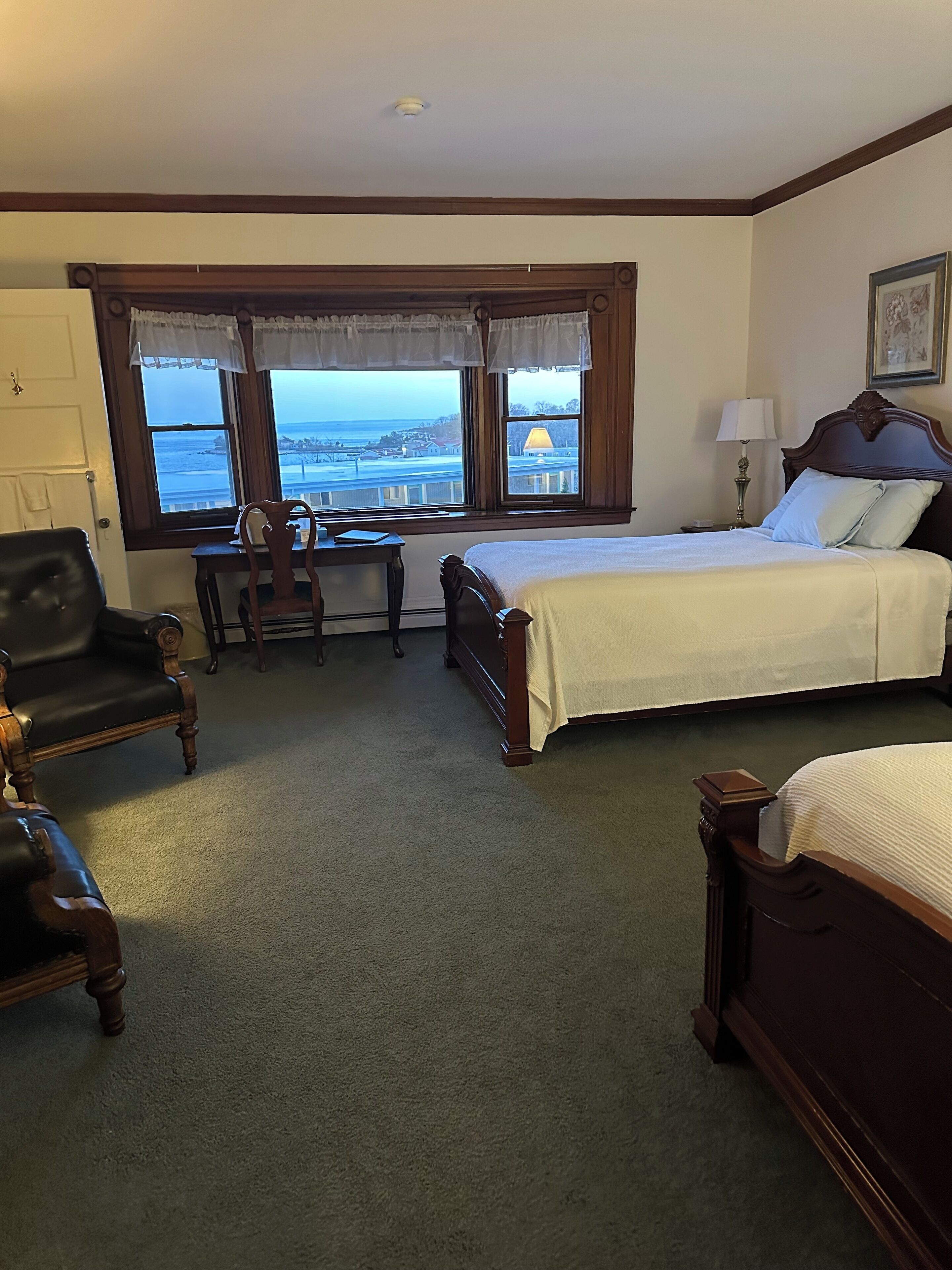 A hotel room with a large bed, a desk with a chair, a view of the ocean, and a wooden headboard.