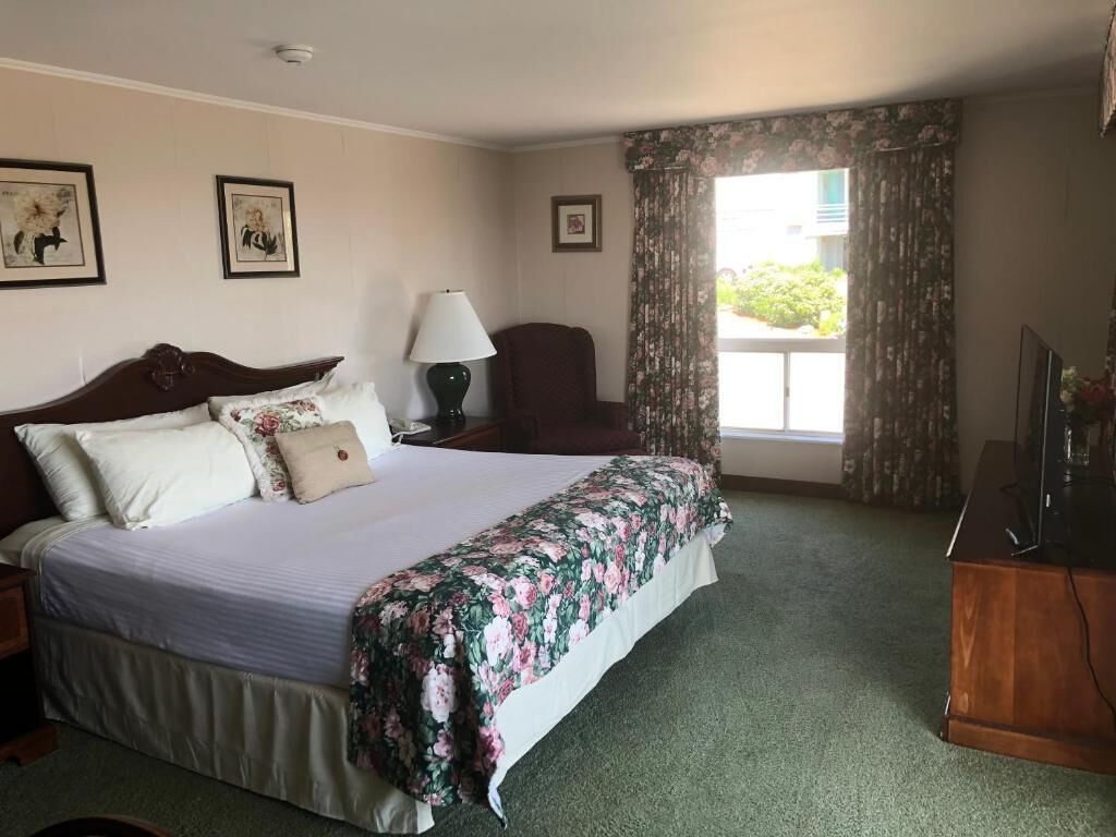 Habitación de hotel con una cama grande, un escritorio con lámpara, una silla, un televisor y una ventana con cortinas.