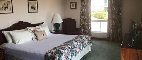 Habitación de hotel con una cama grande, un escritorio con lámpara, una silla, un televisor y una ventana con cortinas.