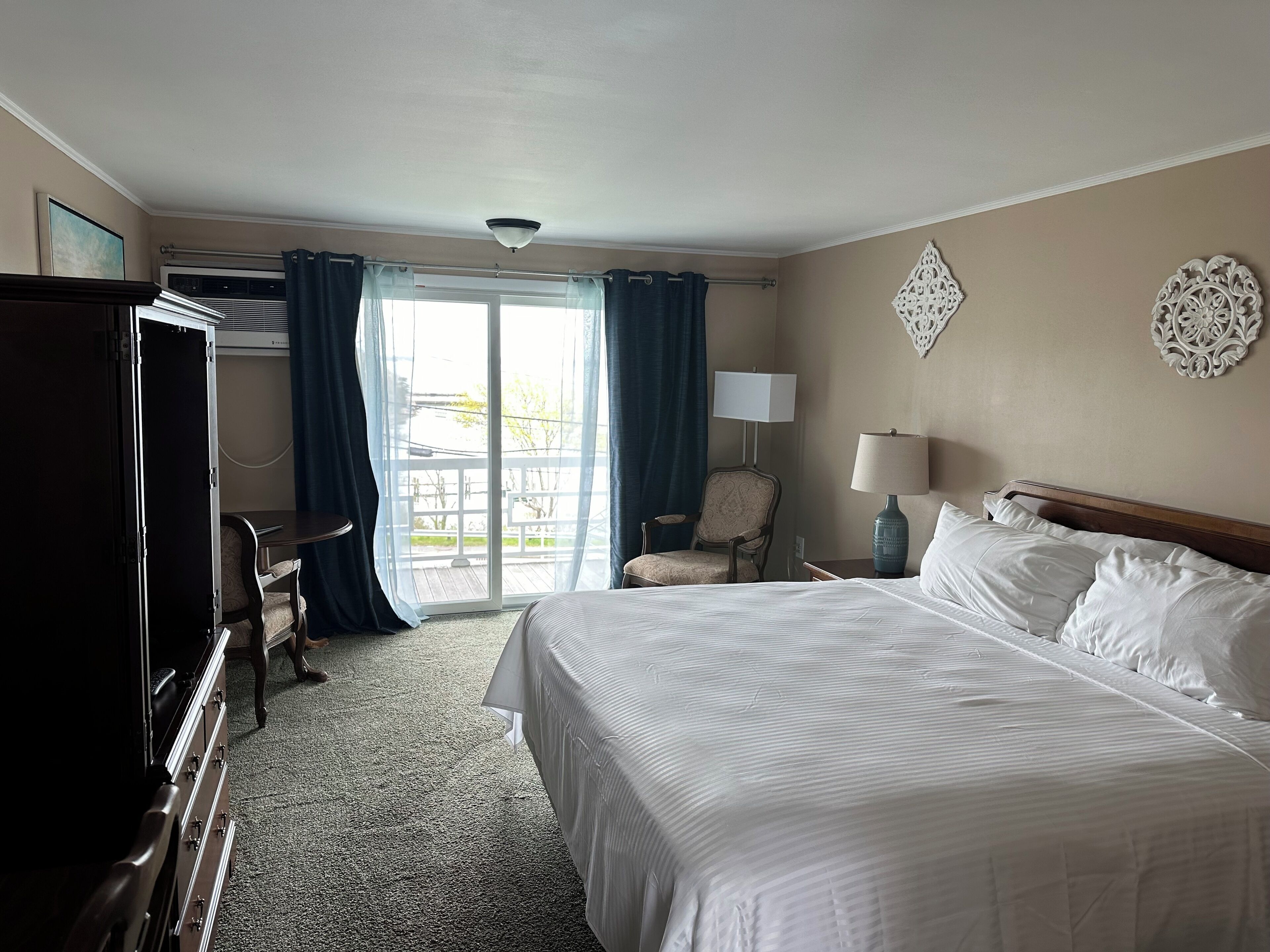 Una habitación de hotel con cama, escritorio, silla, lámpara y vista a través de un ventanal grande.
