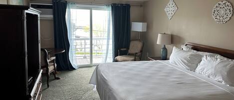 Una habitación de hotel con cama, escritorio, silla, lámpara y vista a través de un ventanal grande.