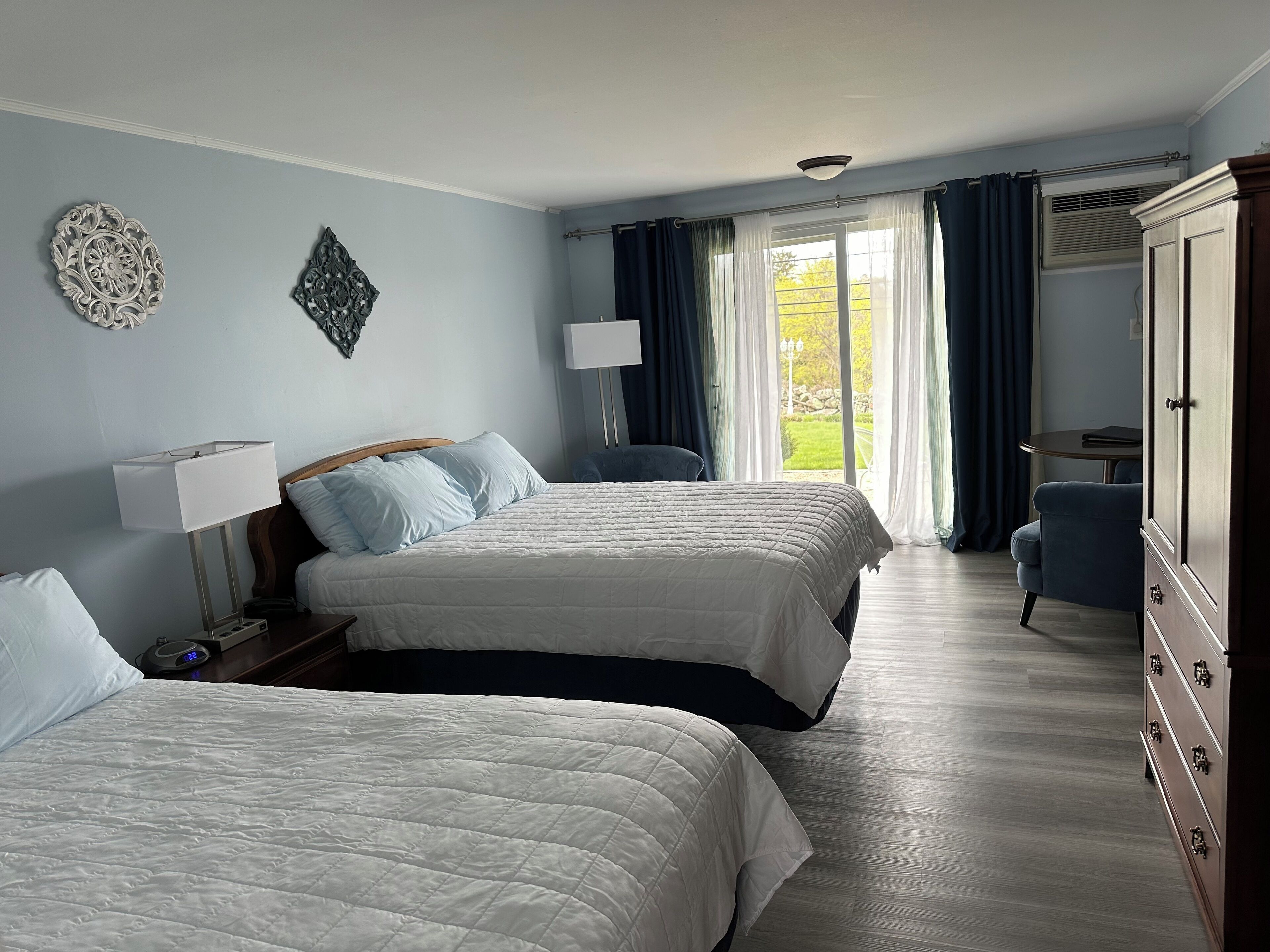 Een hotelkamer met twee bedden, een bureau, een stoel, een kledingkast en een raam met gordijnen.