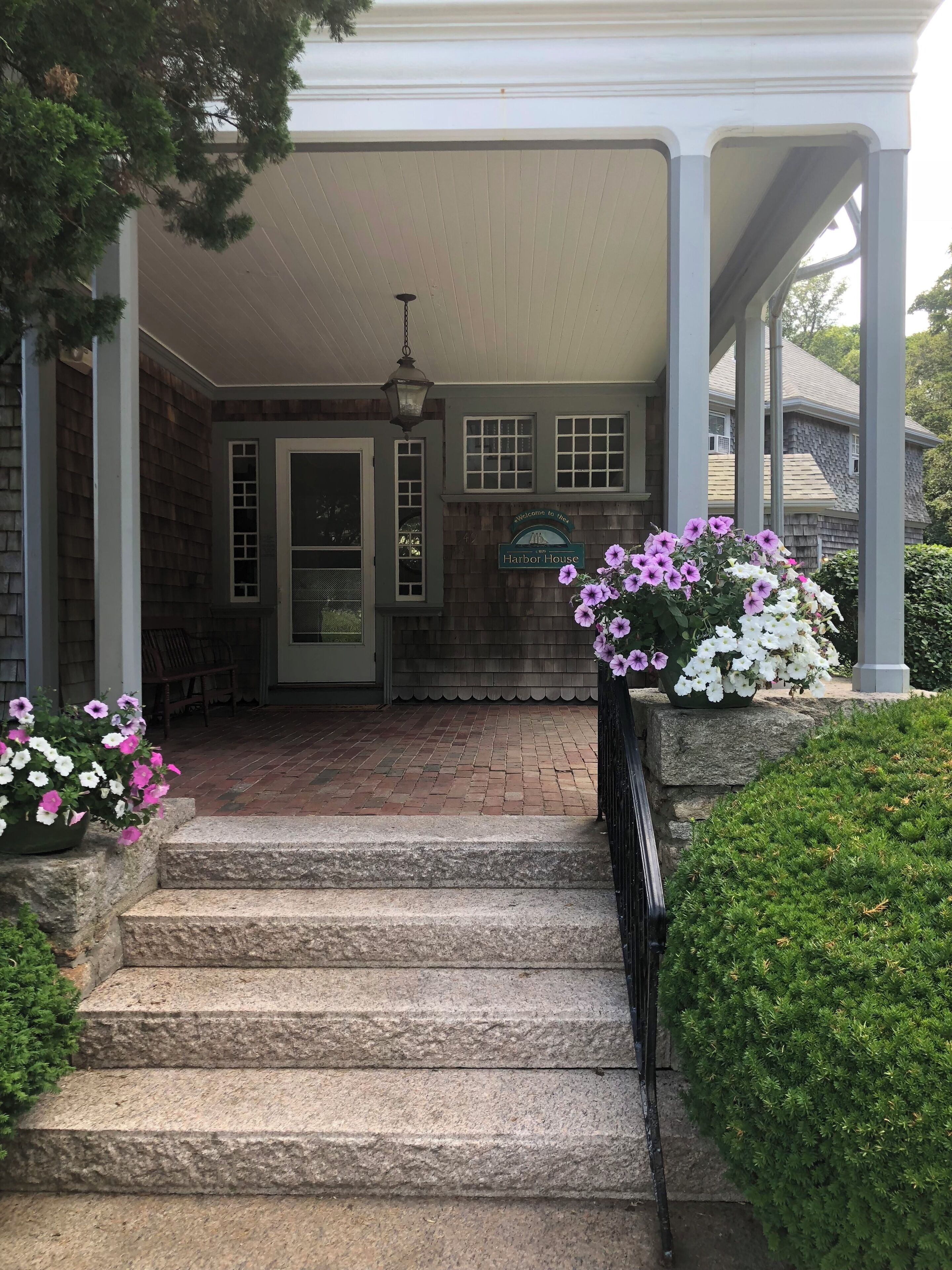 A covered porch with stone steps leading to a door, surrounded by potted flowers and greenery.