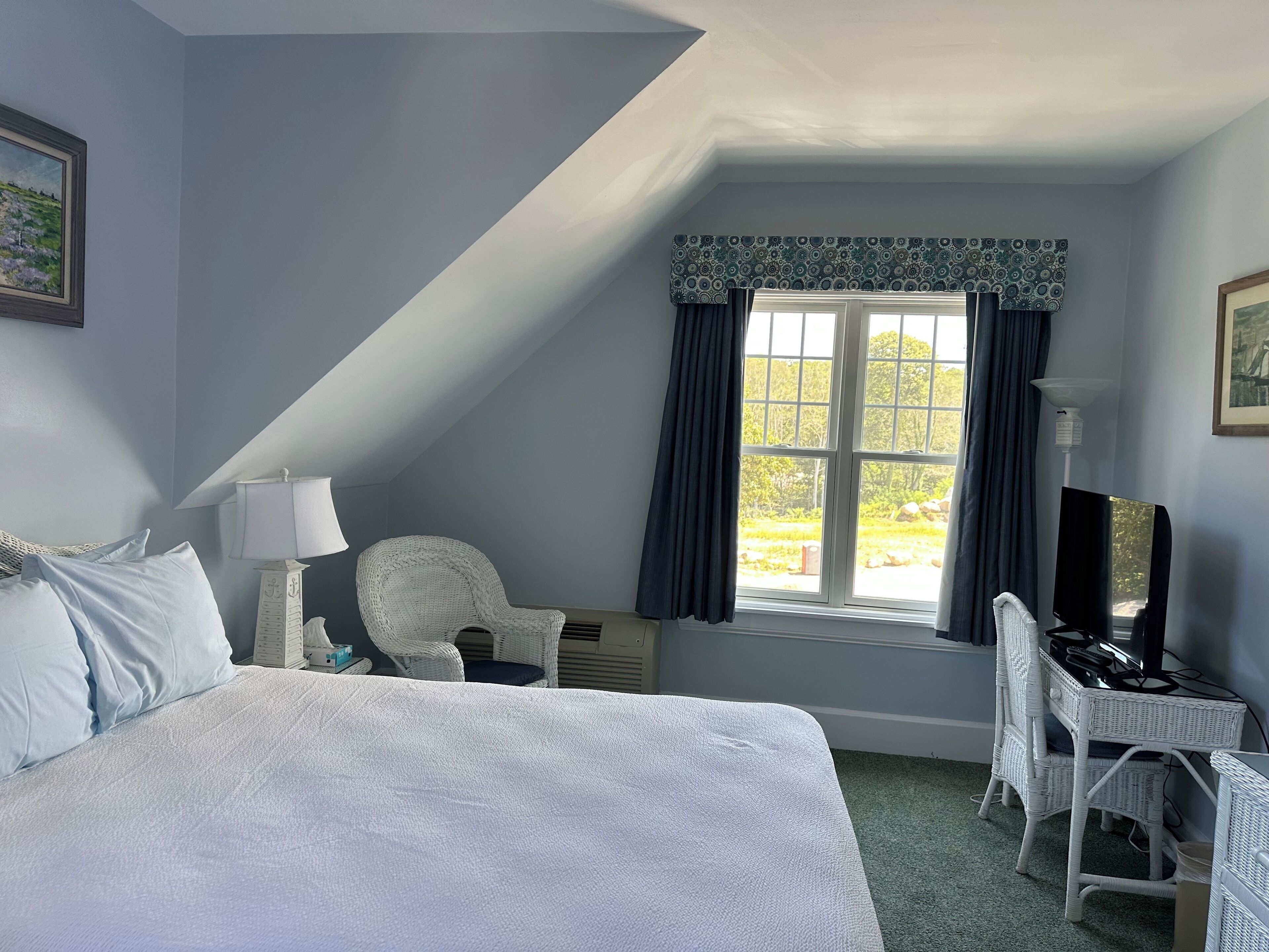 A bedroom with a large bed, a desk with a computer, a chair, a lamp, and a window with curtains.