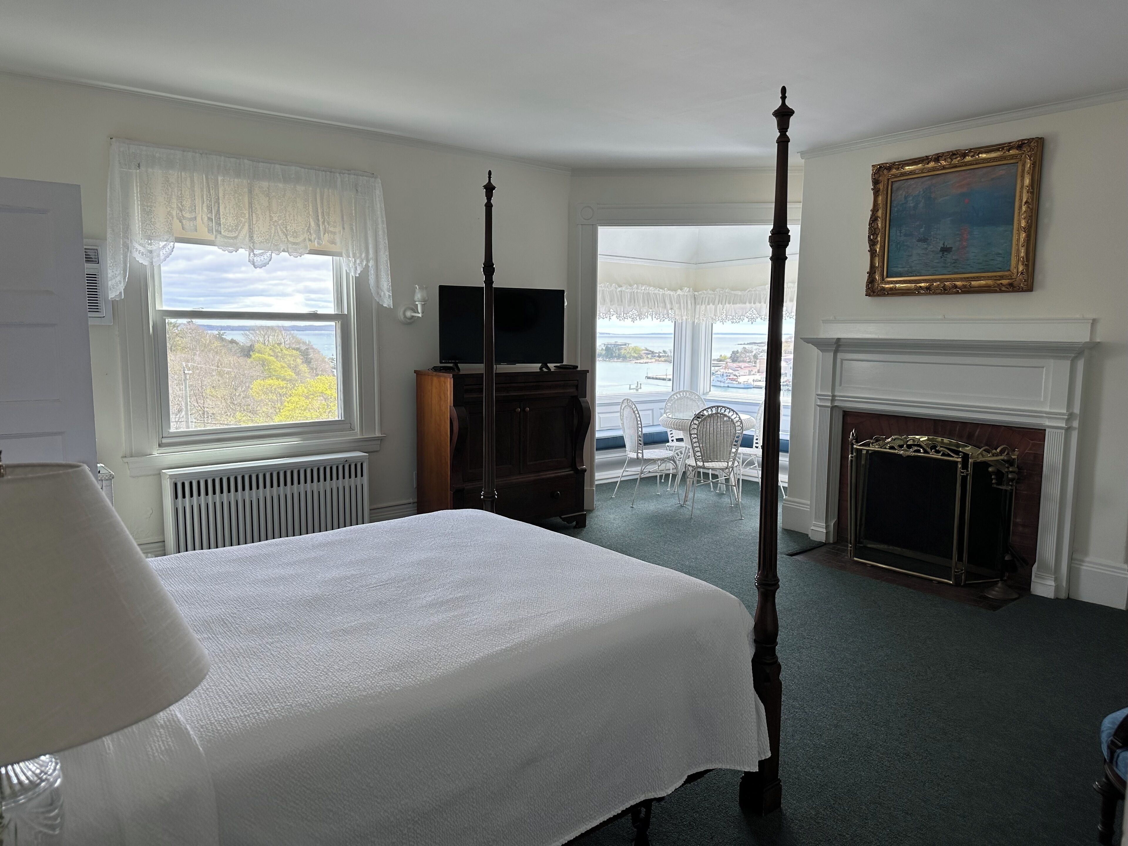 A bedroom with a four-poster bed, a television, a fireplace, and a view of the sea.