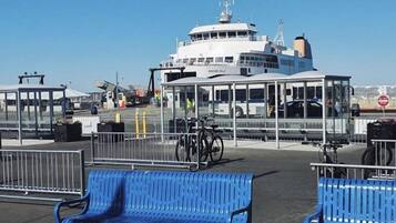 Um terminal de ferry com cobertura de vidro, bancos azuis e um ferry branco atracado no cais.