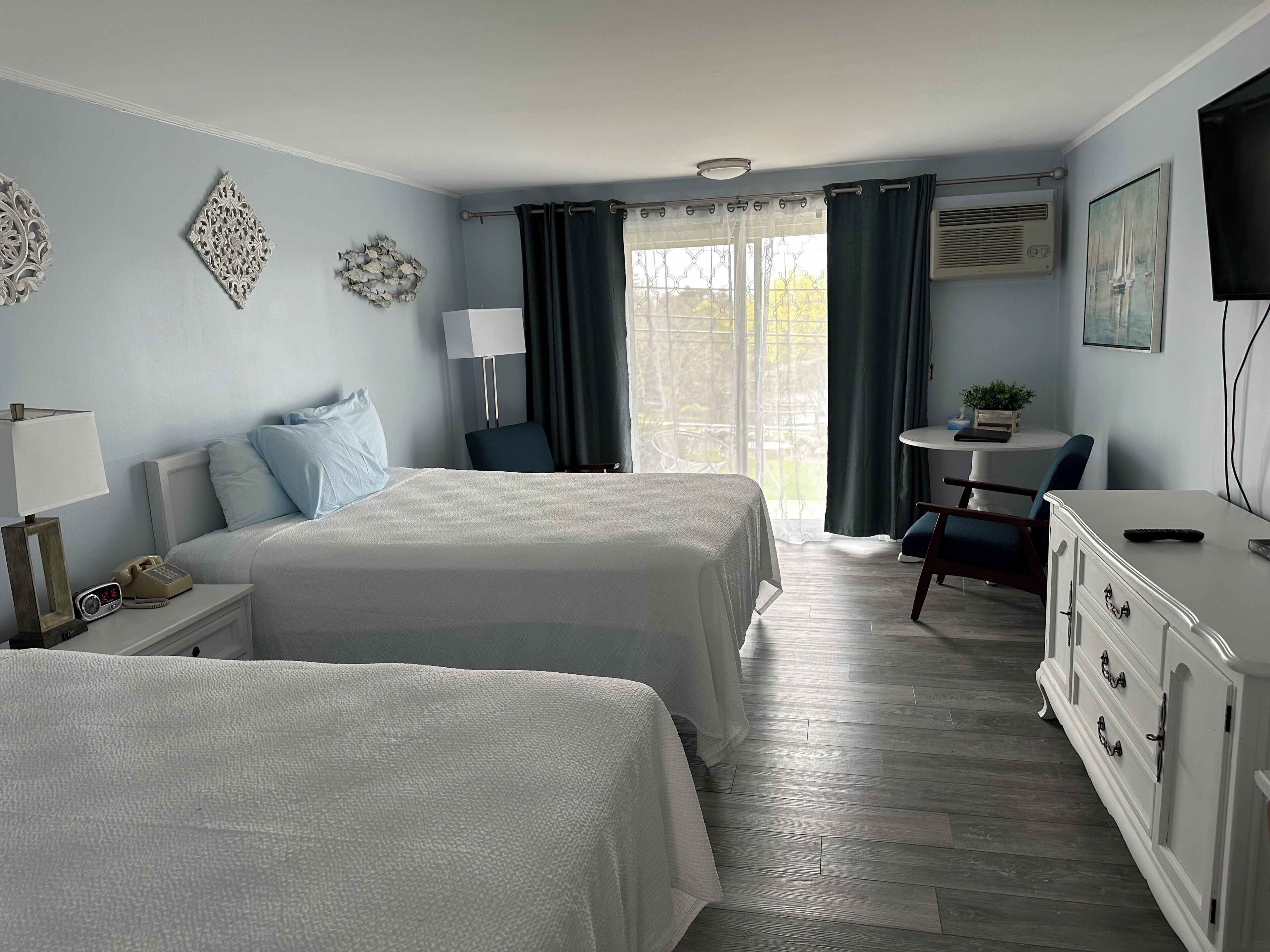 A hotel room with two beds, a desk, a chair, a TV, and a window with curtains.