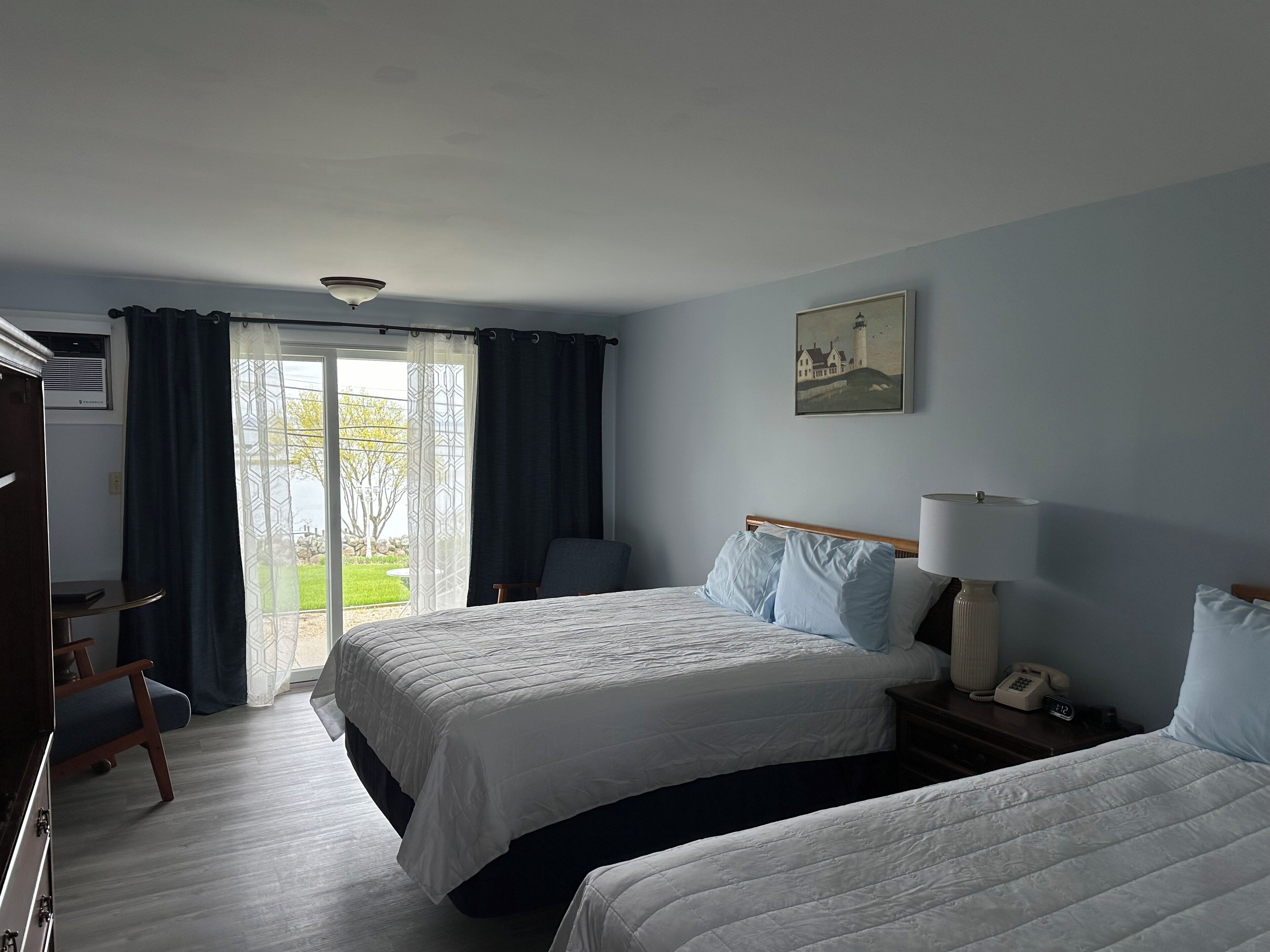 Une chambre d’hôtel avec deux lits, un bureau, une chaise, une lampe et un tableau au mur.