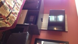 A room with a bed, a desk, a chair, a TV, and a window. - Budget Inn (Tonawanda)