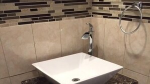 A bathroom with a white sink, dark marble countertop, and tiled walls. - Budget Inn (Tonawanda)