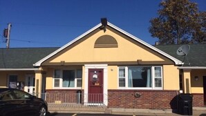 A two-story building with a yellow facade, a red door, and a satellite dish on the roof. - Budget Inn (Tonawanda)