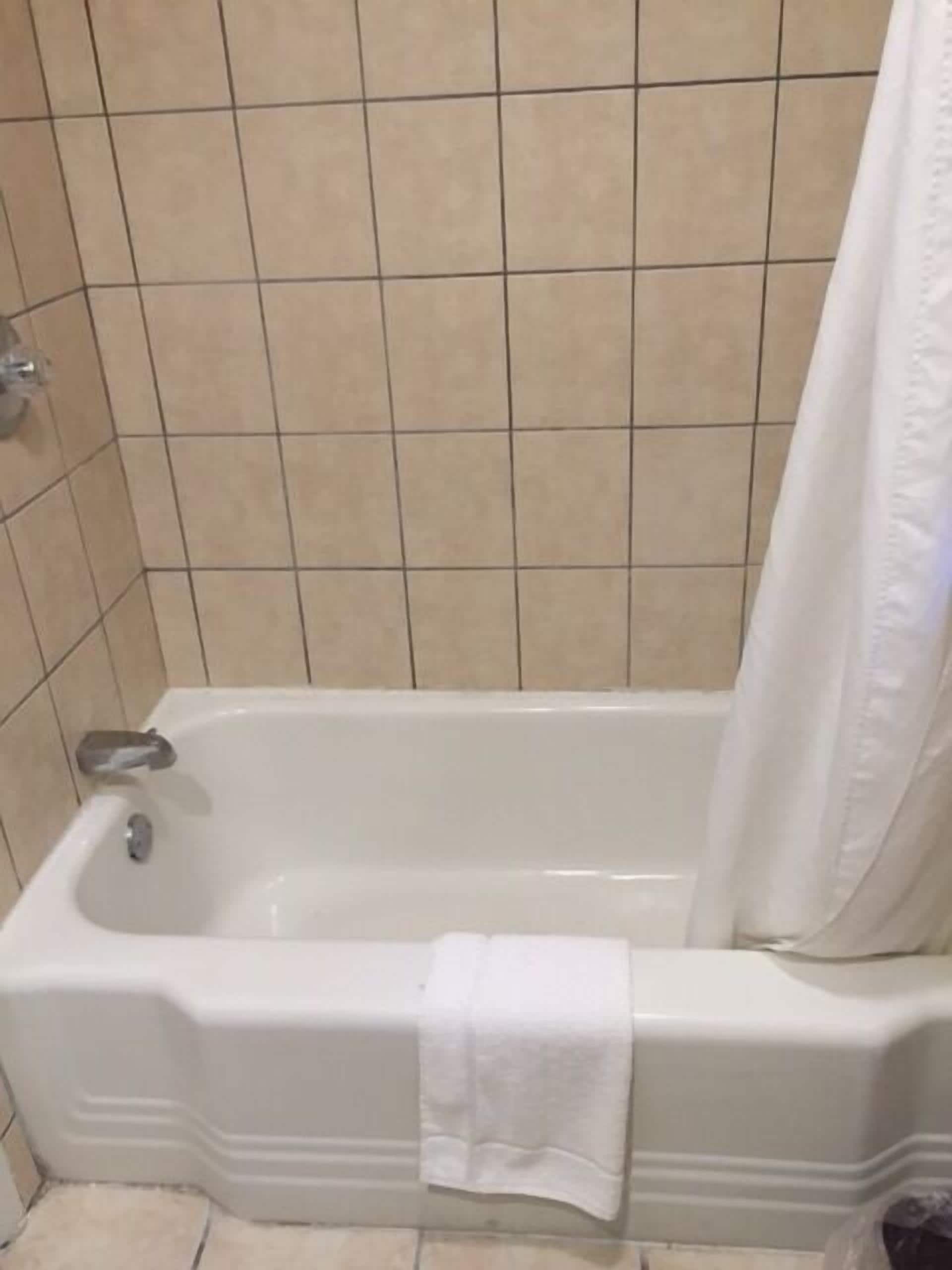 Una bañera blanca estándar con cortina de ducha, una toalla blanca colgada al lado y paredes de azulejos color beige.