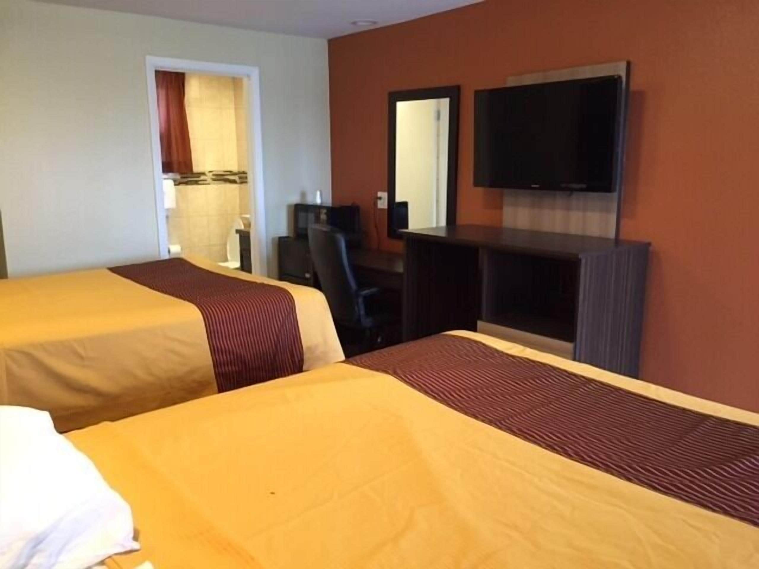 A hotel room with two beds, a desk, a chair, a television, and a mirror.