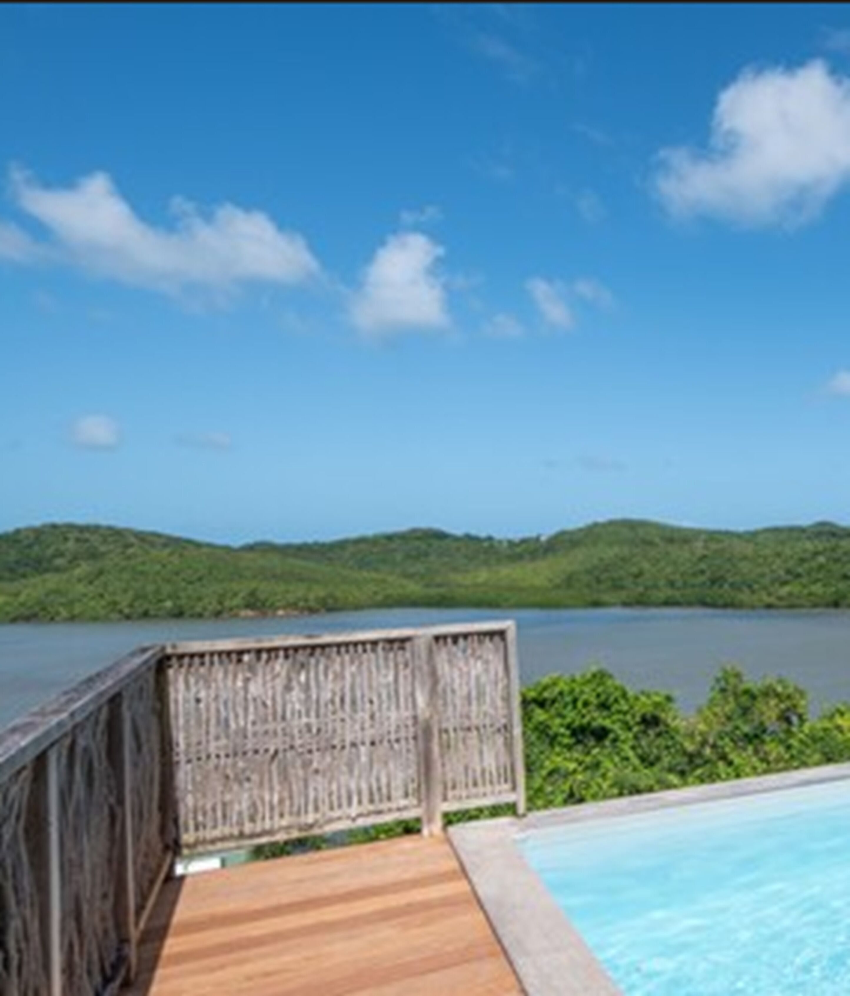 Eine Holzterrasse mit Blick auf einen Swimmingpool und eine Seenlandschaft mit fernen Hügeln.