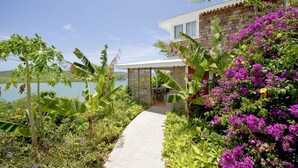 A pathway leading to a house with a view of a lake, surrounded by lush greenery and vibrant flowers. - Hôtel Plein Soleil (Le Francois)