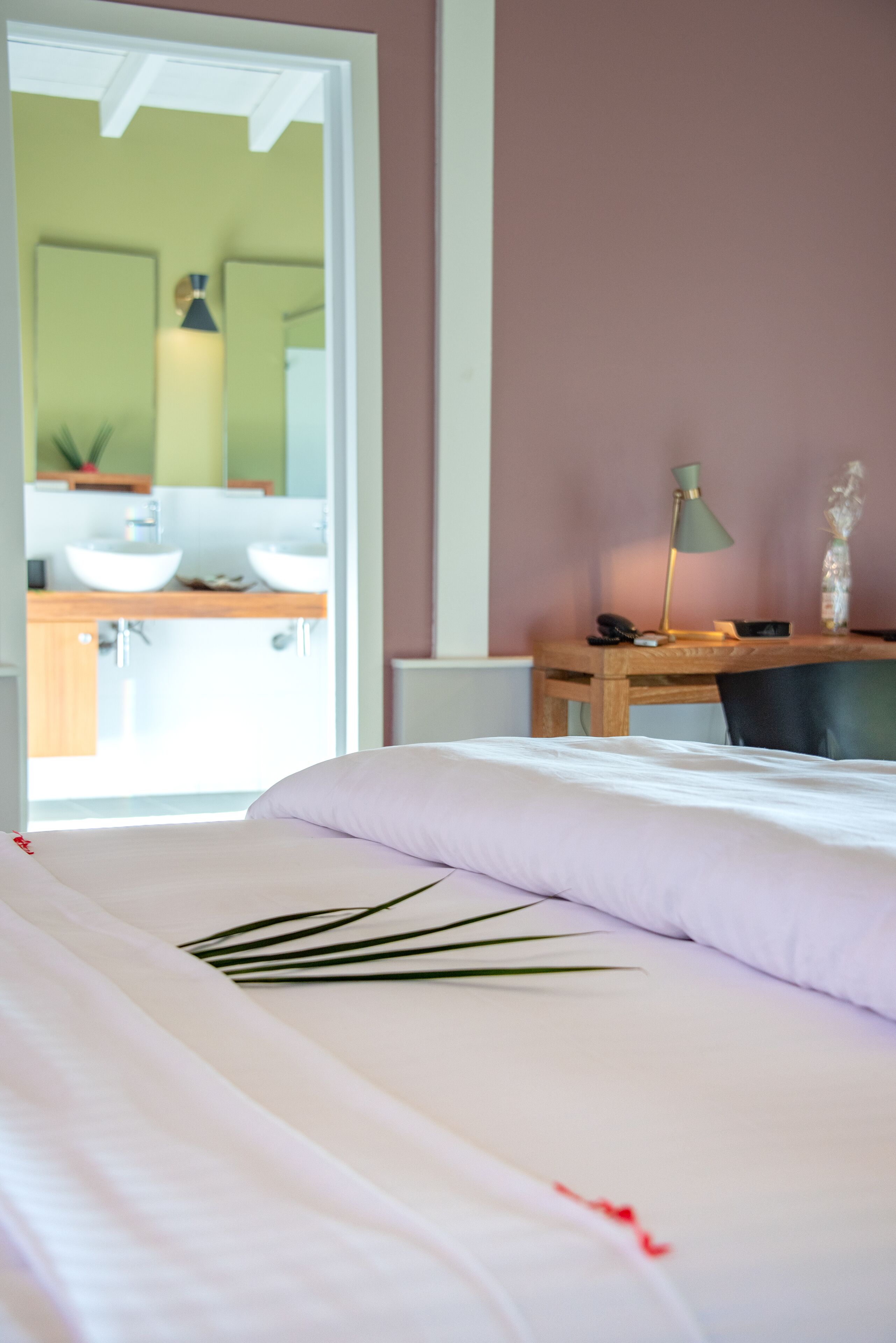 A bedroom with a bed, a desk, a chair, and a bathroom visible through an open door.
