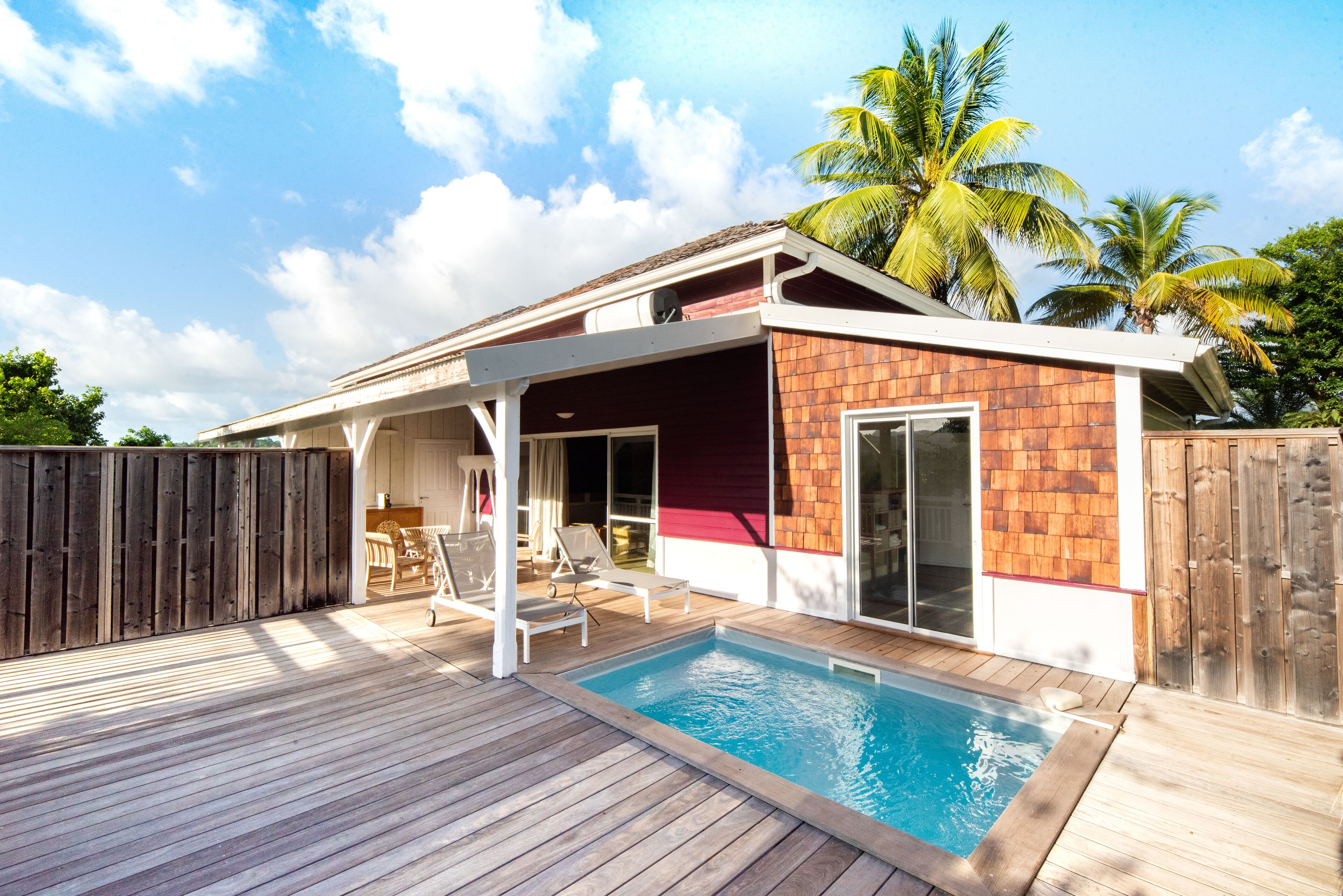 A poolside area with a wooden deck, a pool, and a covered patio with lounge chairs.