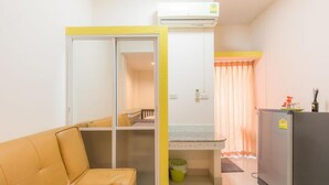 Un espacio habitable compacto con sofá, kitchenette y una puerta corredera que da a un dormitorio.